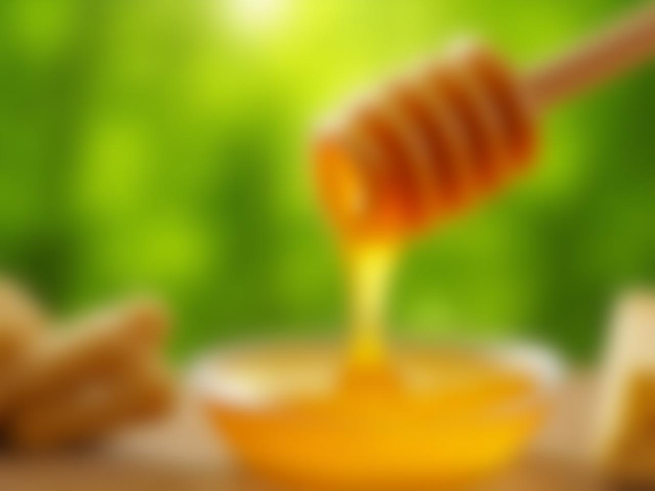 Close-up of golden raw honey dripping from a wooden dipper, with a blurred background of lush green forest.